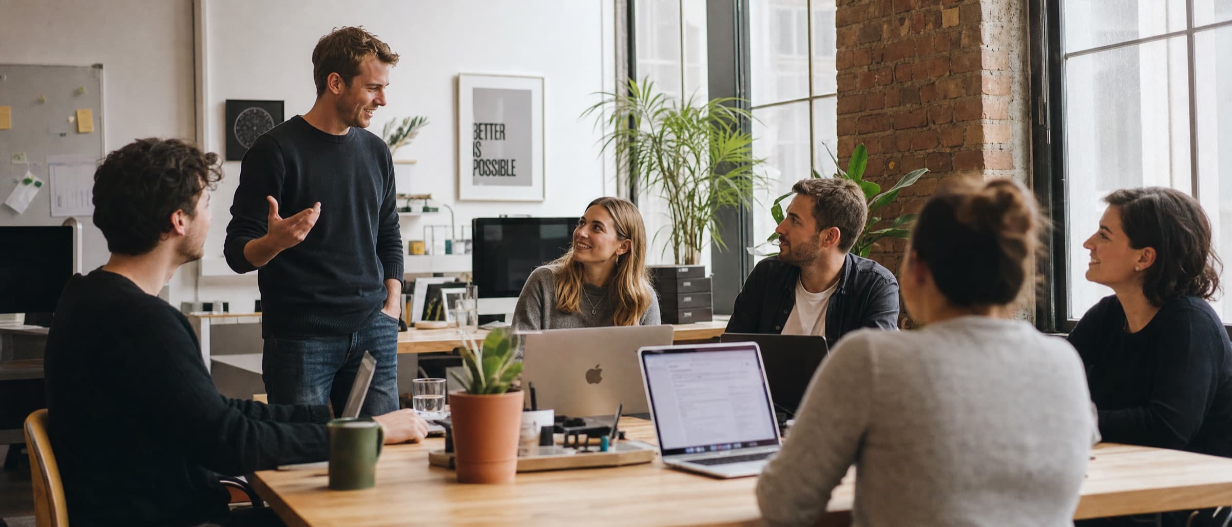 A small team talking around a long table in a bright open-plan office